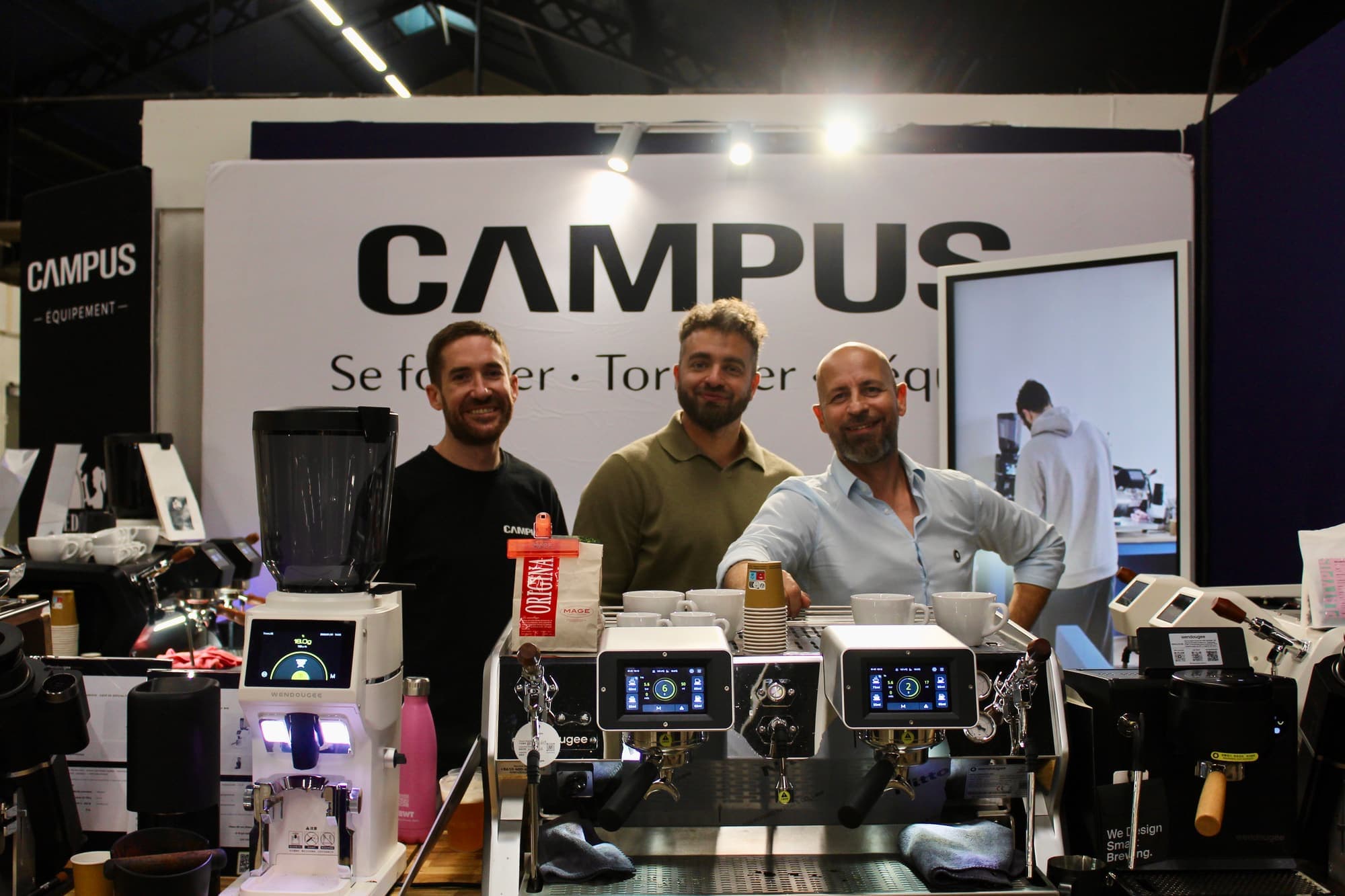 Les trois associés de CAMPUS derrière le comptoir de leur stand, devant l’enseigne « Se former · Torréfier · S’équiper »